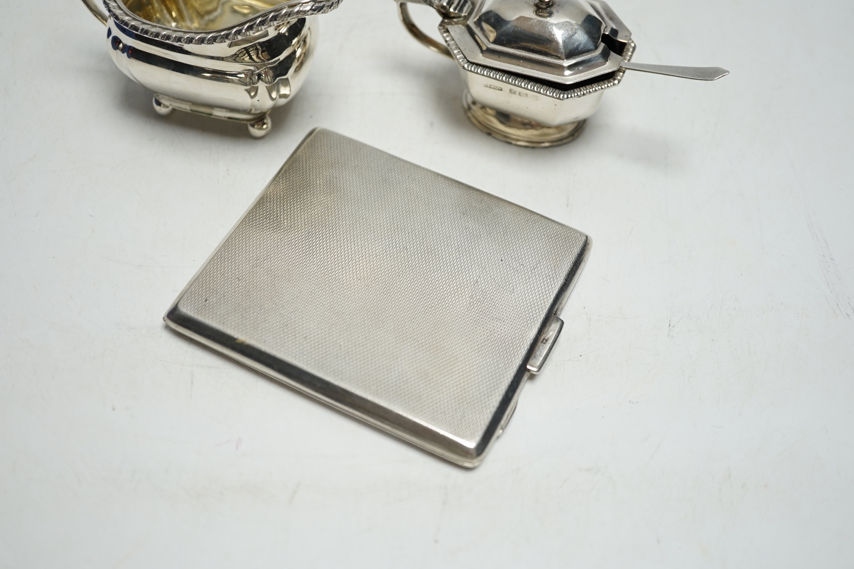 A George VI engine turned silver cigarette case, a silver lidded mustard pot and a small silver cream jug.